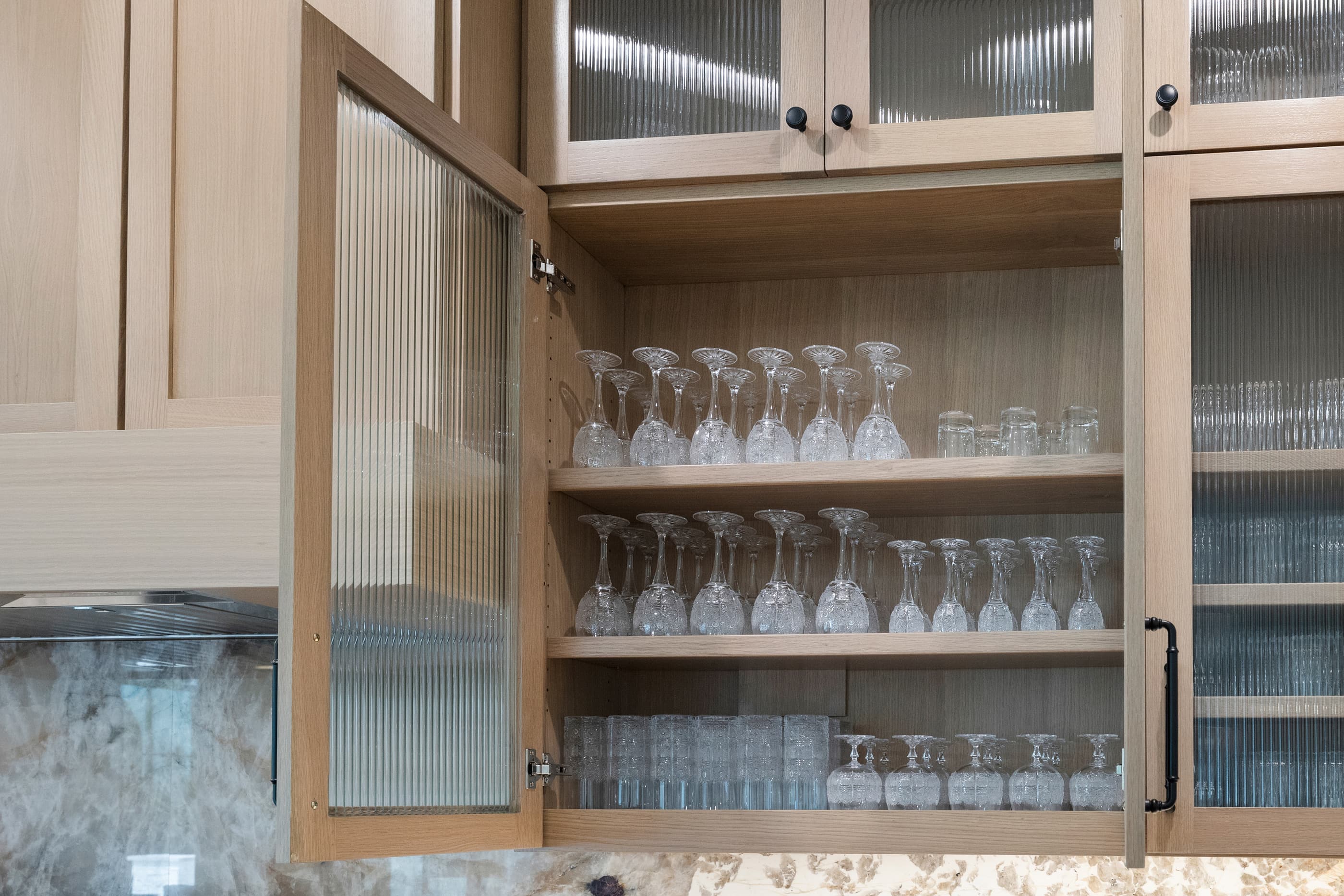 Open reeded-glass kitchen cabinet storing stemware and glasses on lit shelves