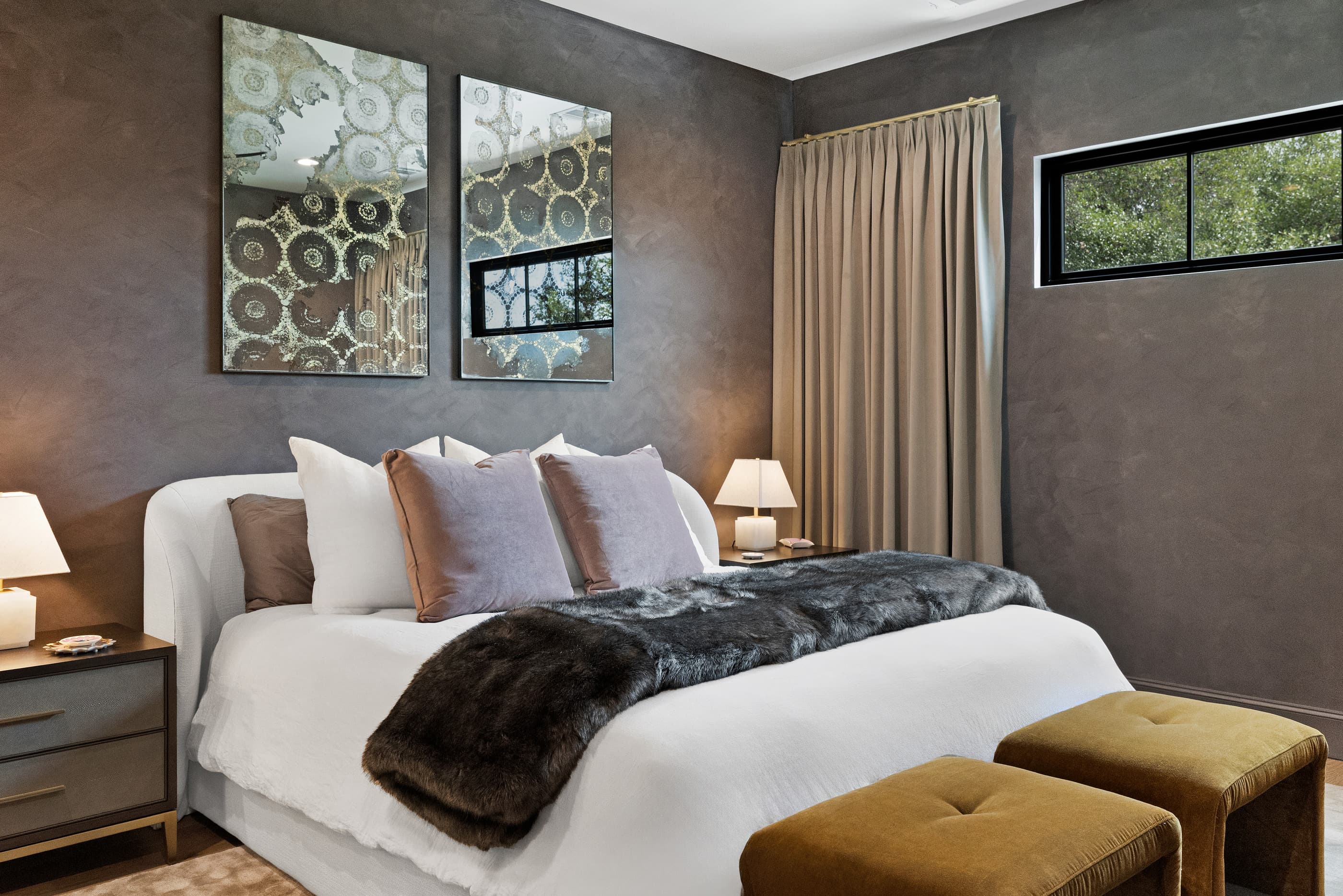 Primary bedroom with plaster-finish walls, upholstered bed with faux-fur throw and gold velvet benches