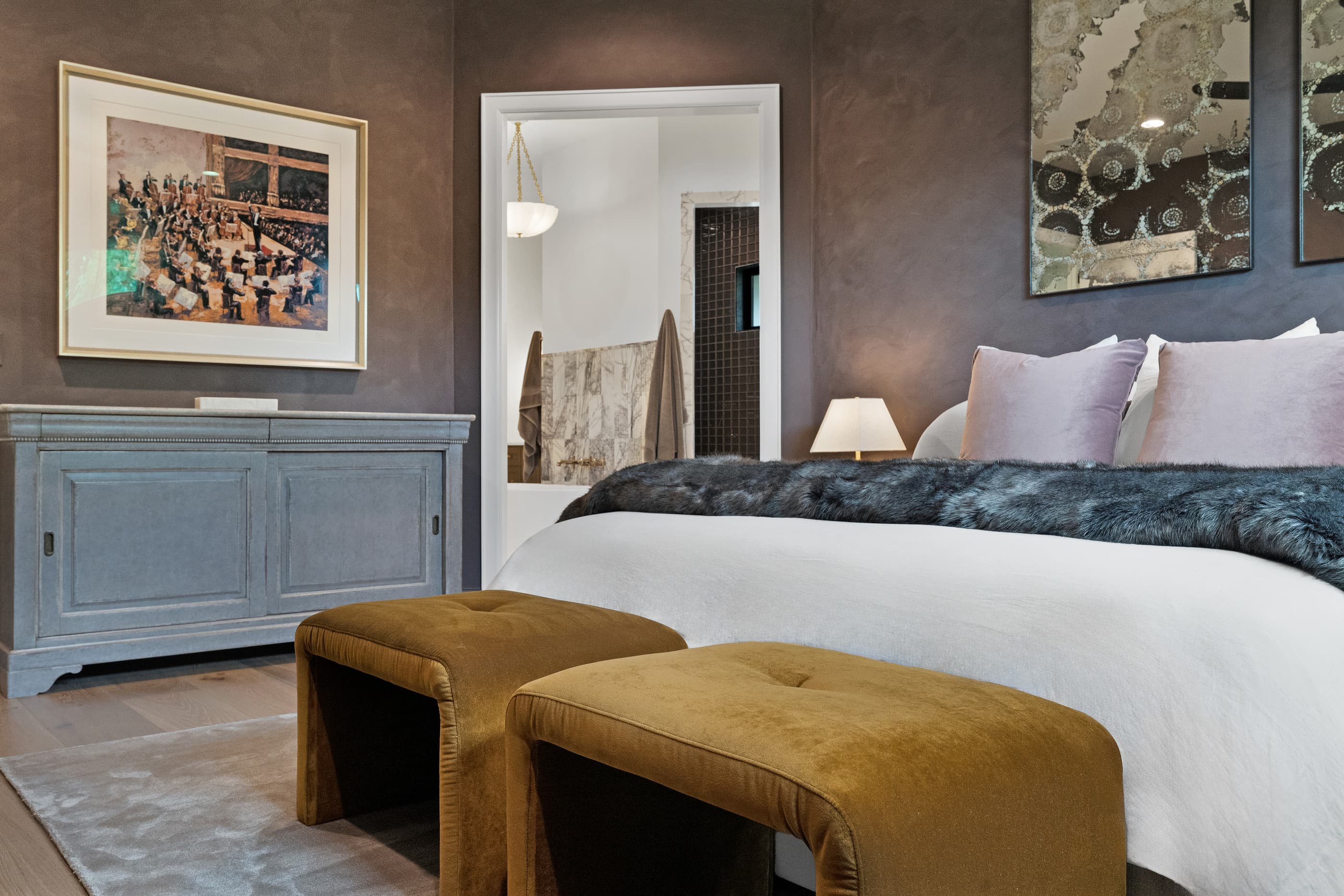 Primary bedroom with a gray dresser, framed art and gold velvet benches at the foot of the bed