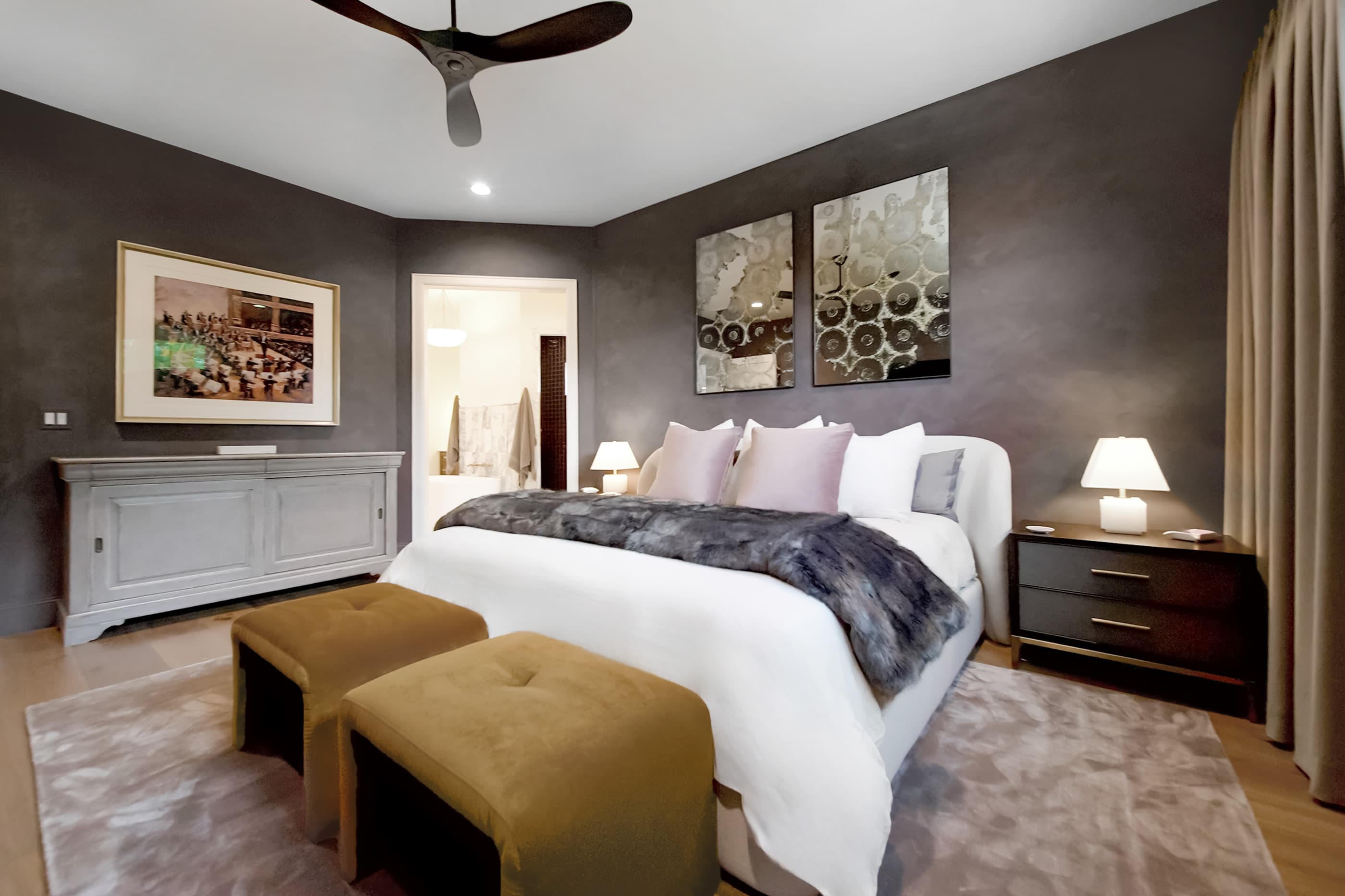 Primary suite with a ceiling fan, mirrored wall art and an open doorway to the bath
