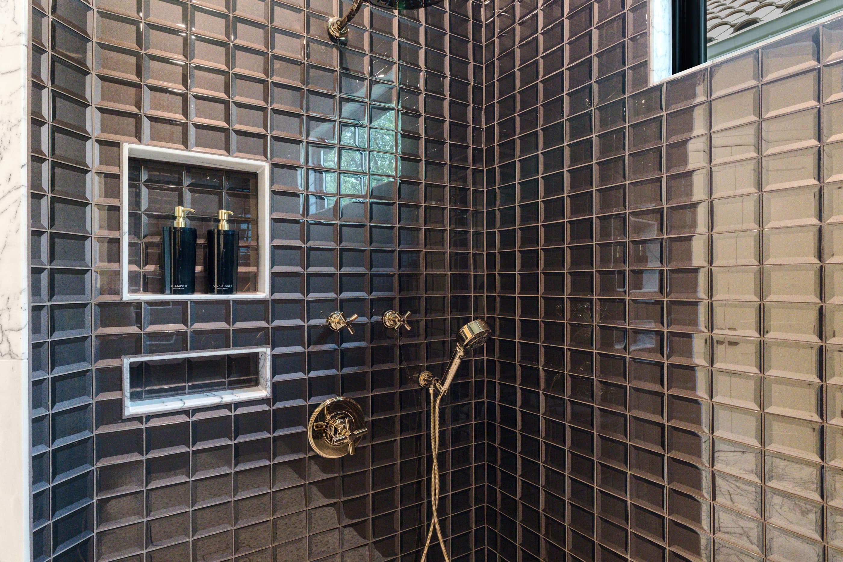 Walk-in shower with dark glossy tile, recessed niches and brass fixtures with a handheld shower