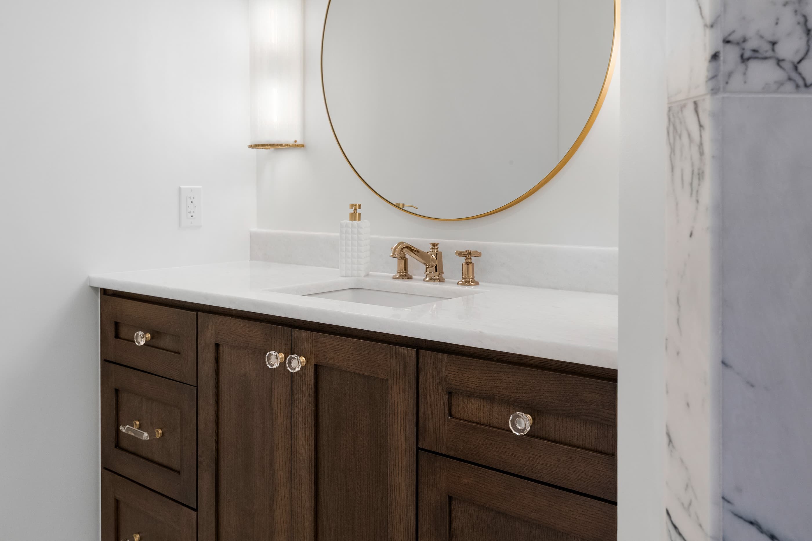 Bathroom vanity in stained wood with brass faucet, undermount sink and round gold-framed mirror
