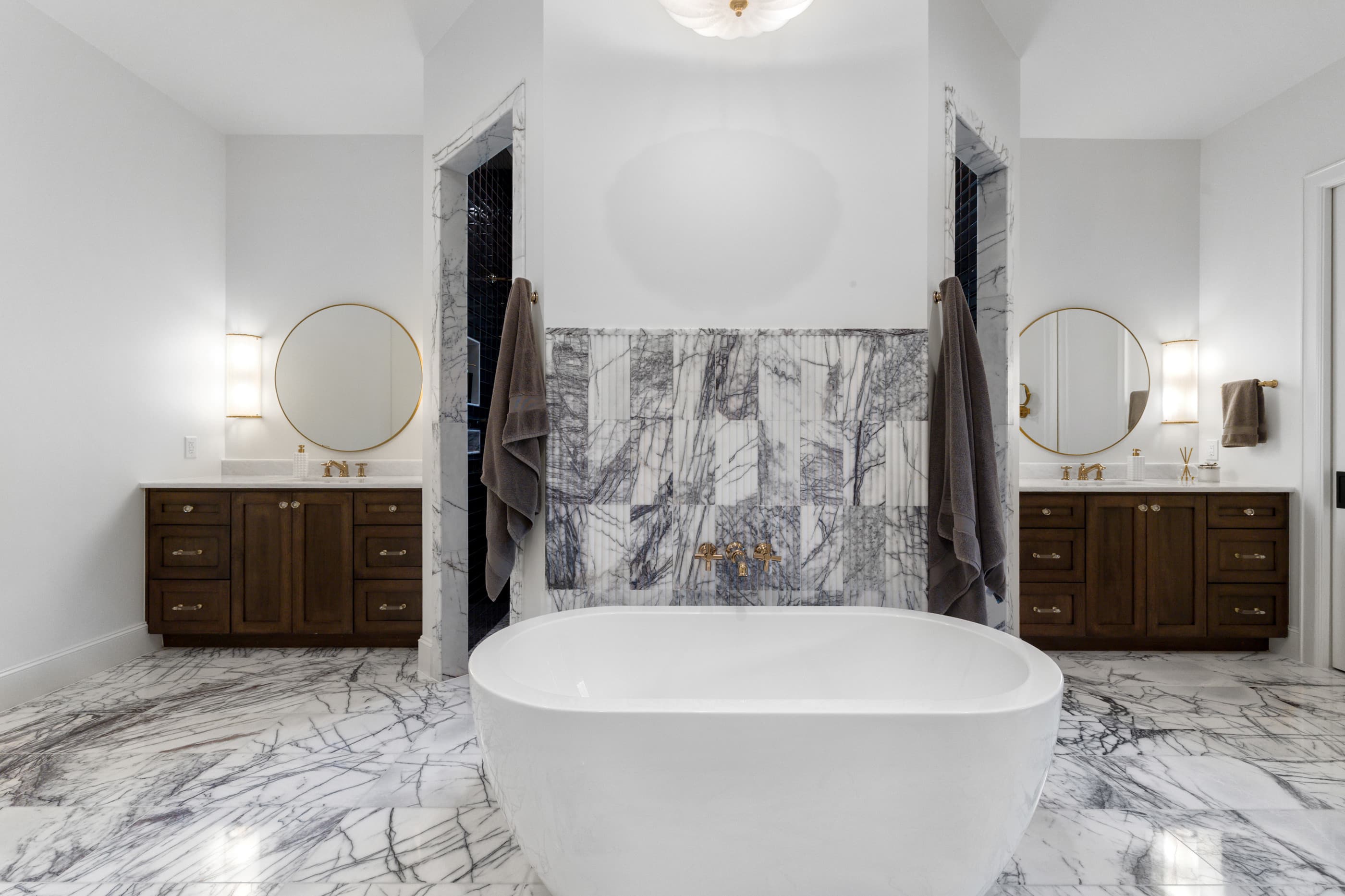 Primary bath with a freestanding tub, marble feature wall and dual wood vanities with round mirrors
