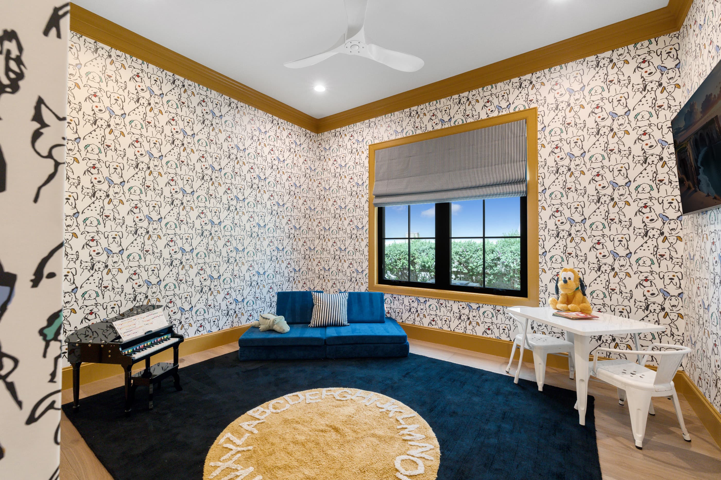 Playroom with patterned wallpaper, gold trim, blue sofa, small piano and children's table