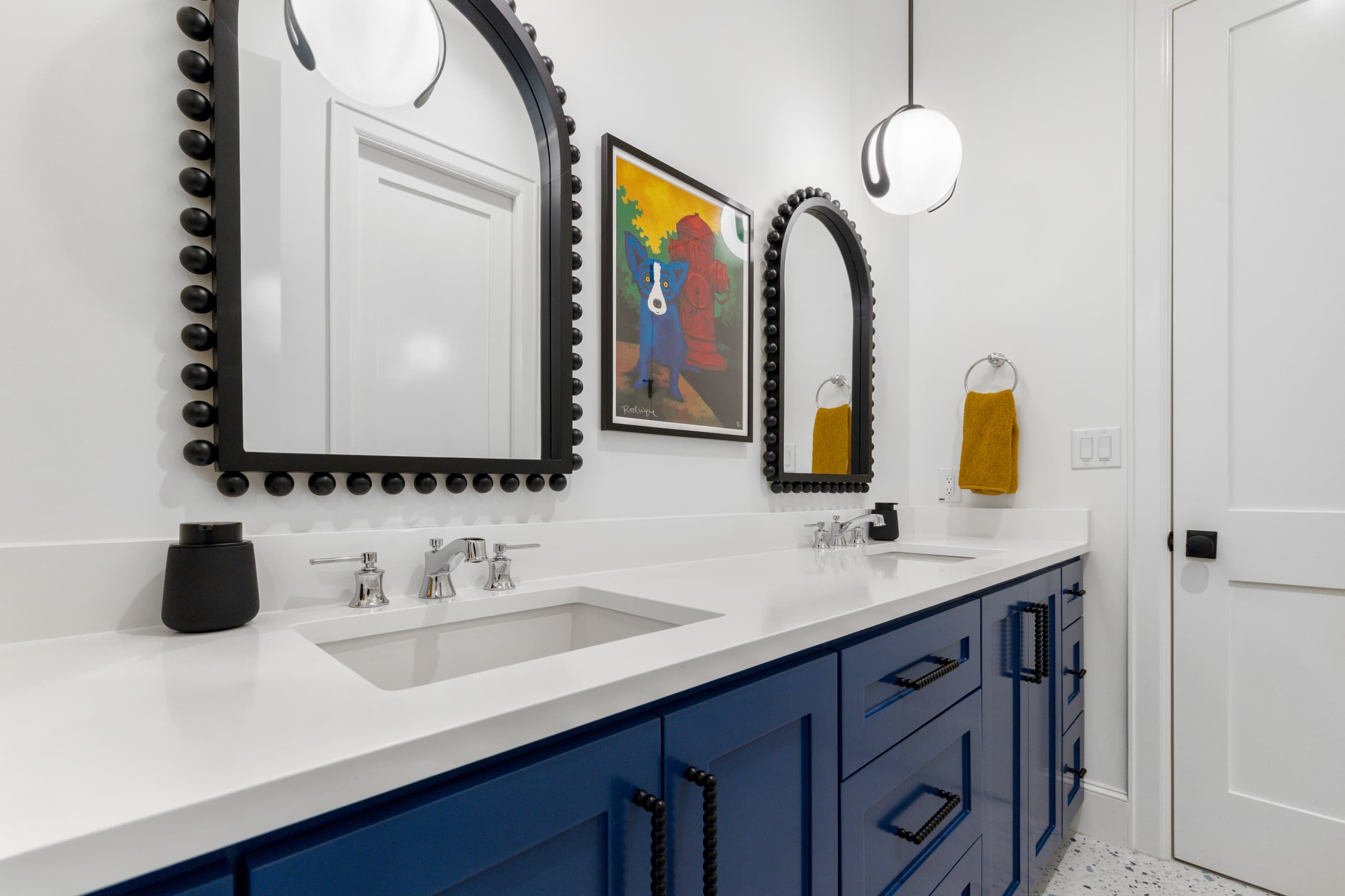Bathroom with a blue cabinet vanity, white quartz counter, beaded black mirrors and brass-accent hardware