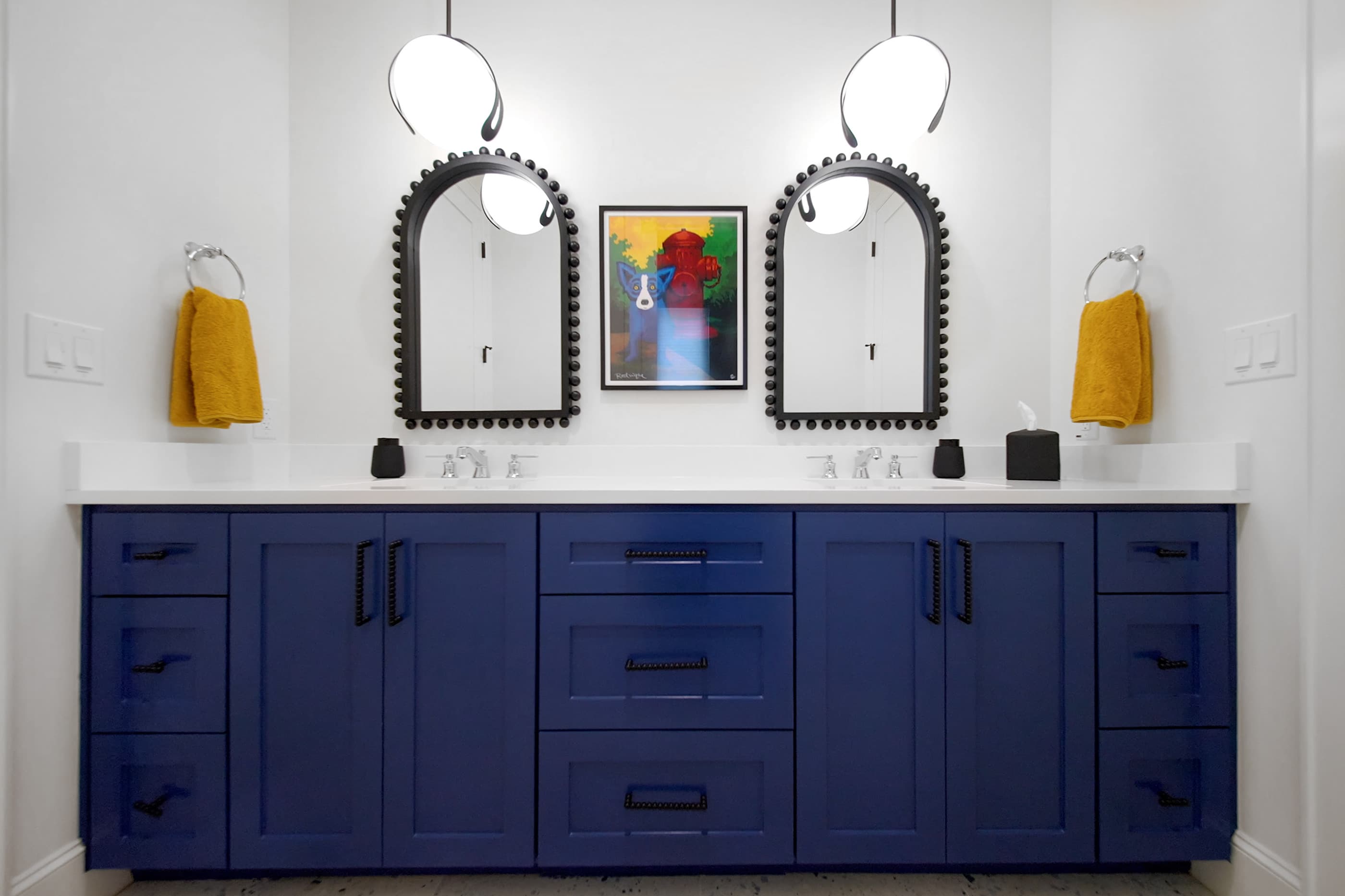 Double-sink bathroom with deep blue cabinetry, arched beaded mirrors and colorful framed art