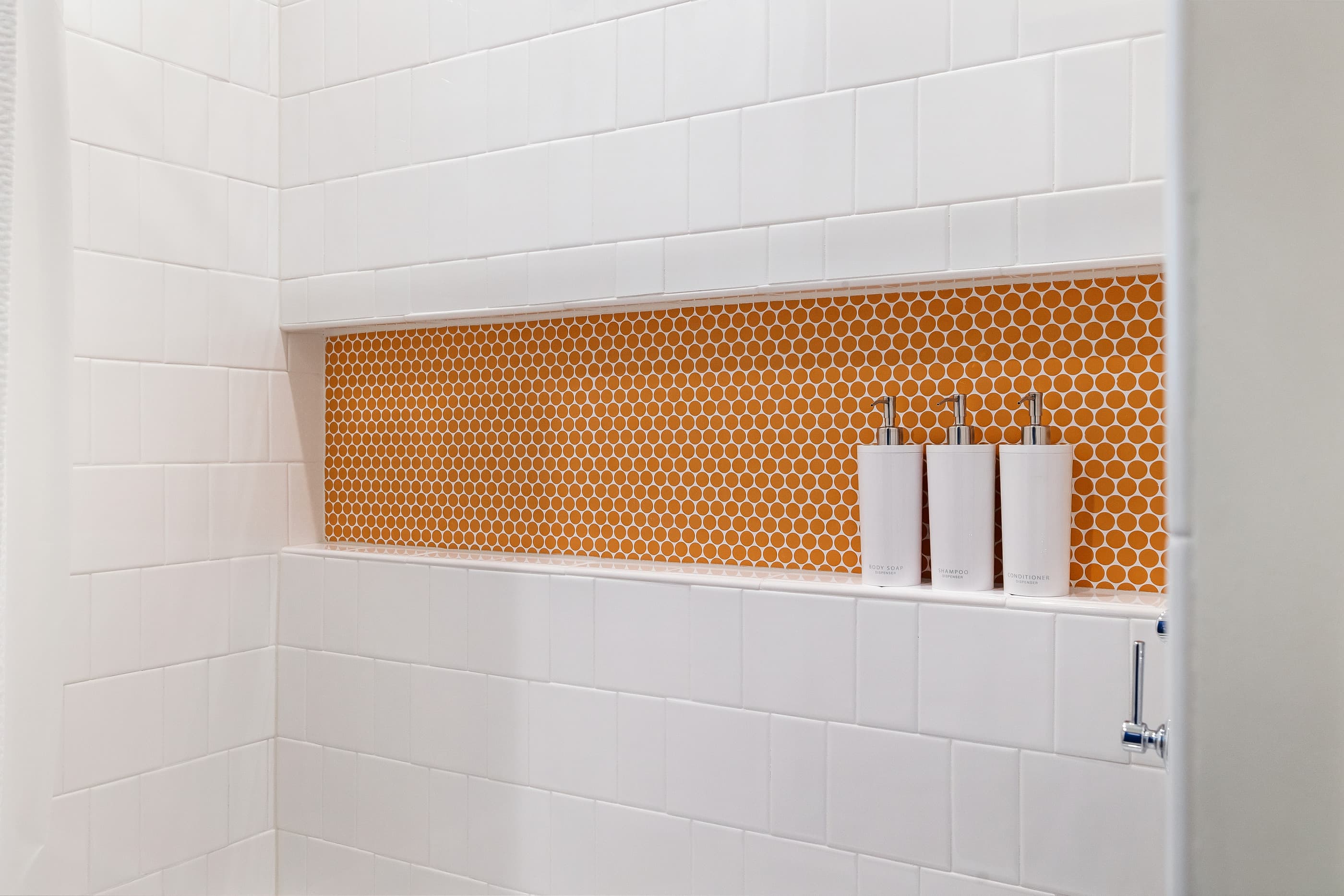 Shower niche with orange hexagon tile set in white square tile