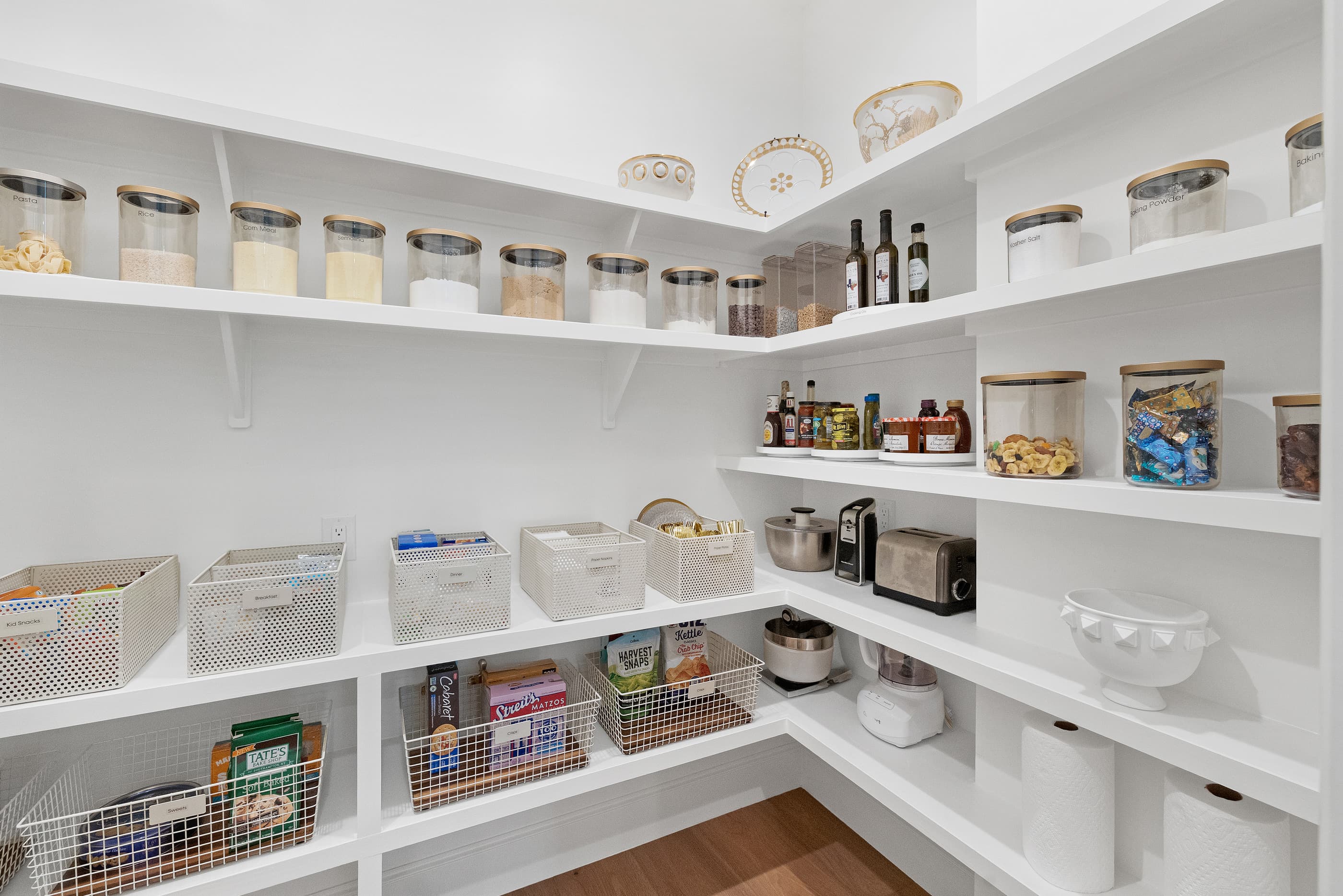 Corner pantry with white shelves, labeled baskets and glass canisters