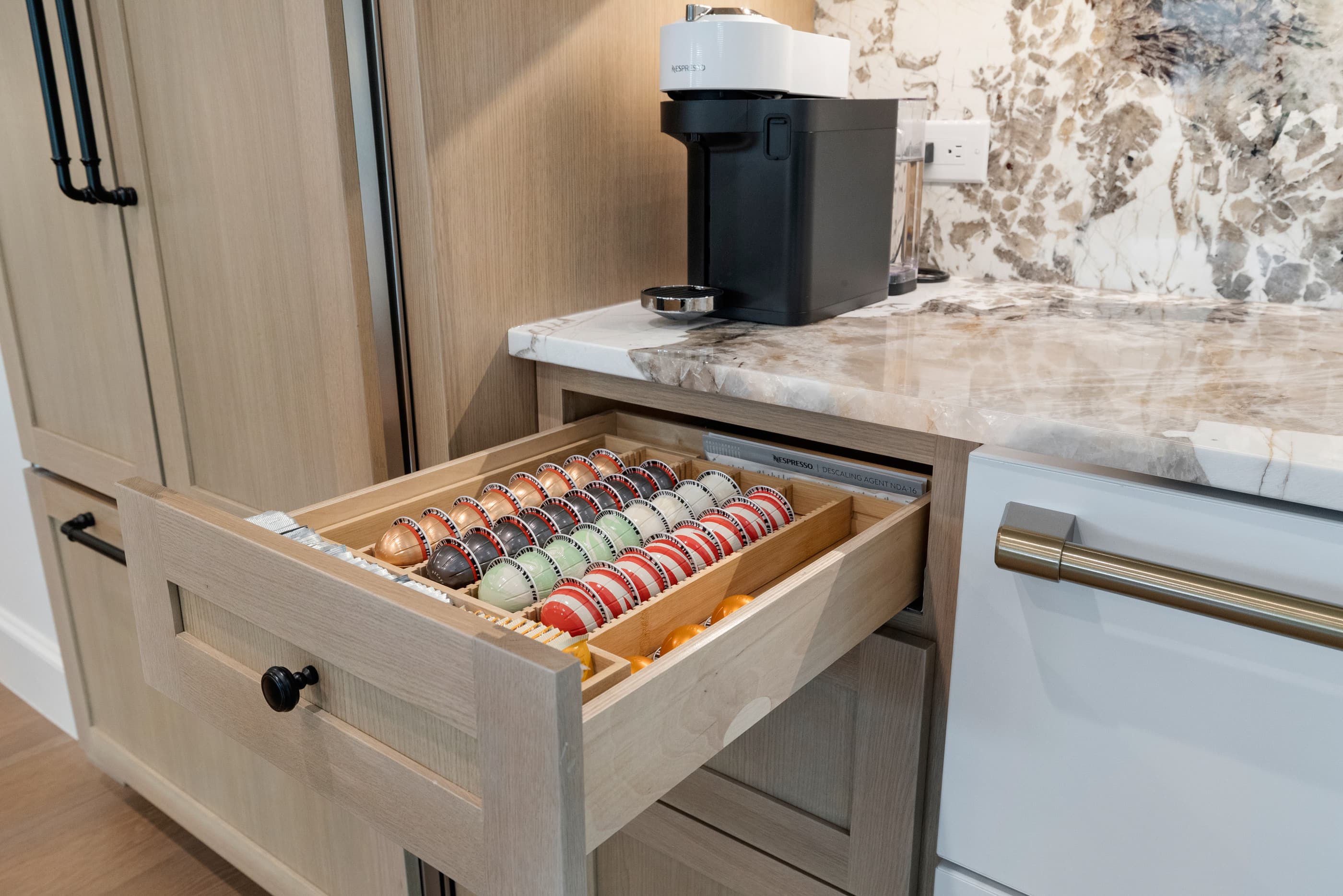 Kitchen drawer with a custom insert organizing coffee capsules beside a coffee maker