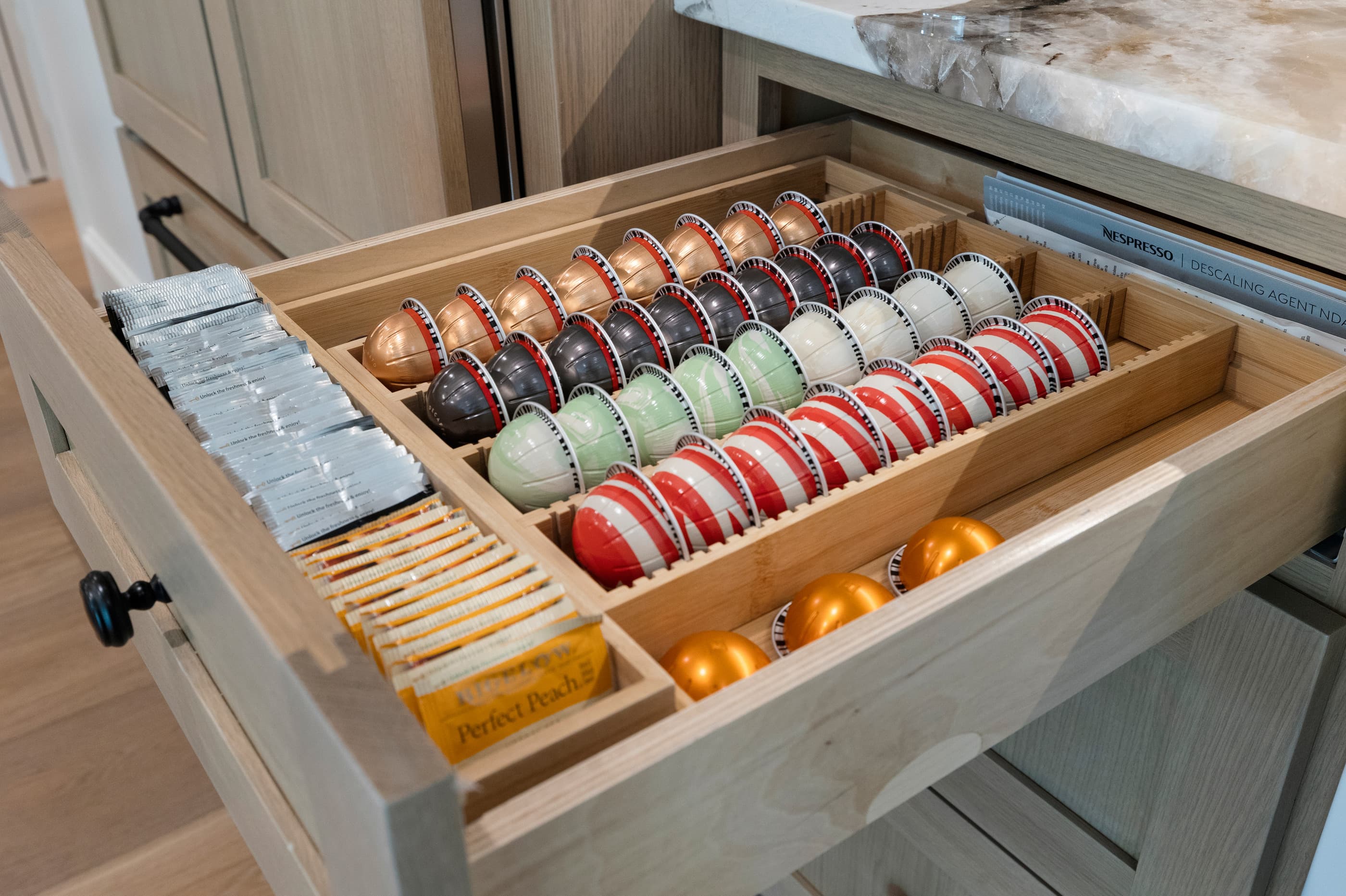 Close-up of a custom drawer insert organizing coffee capsules and tea