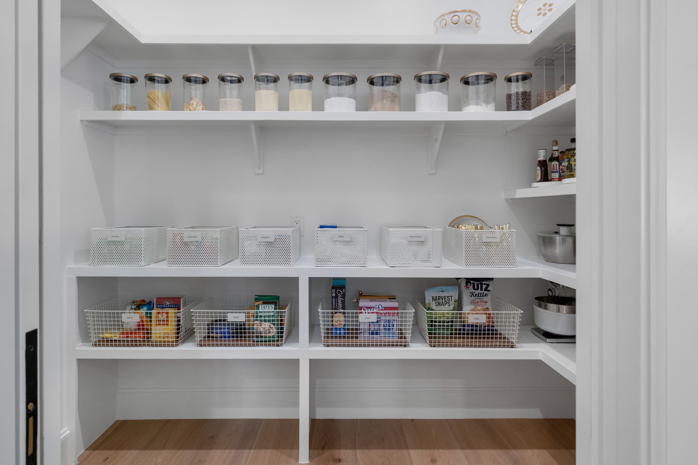 Walk-in pantry with white built-in shelves, wire baskets and canisters