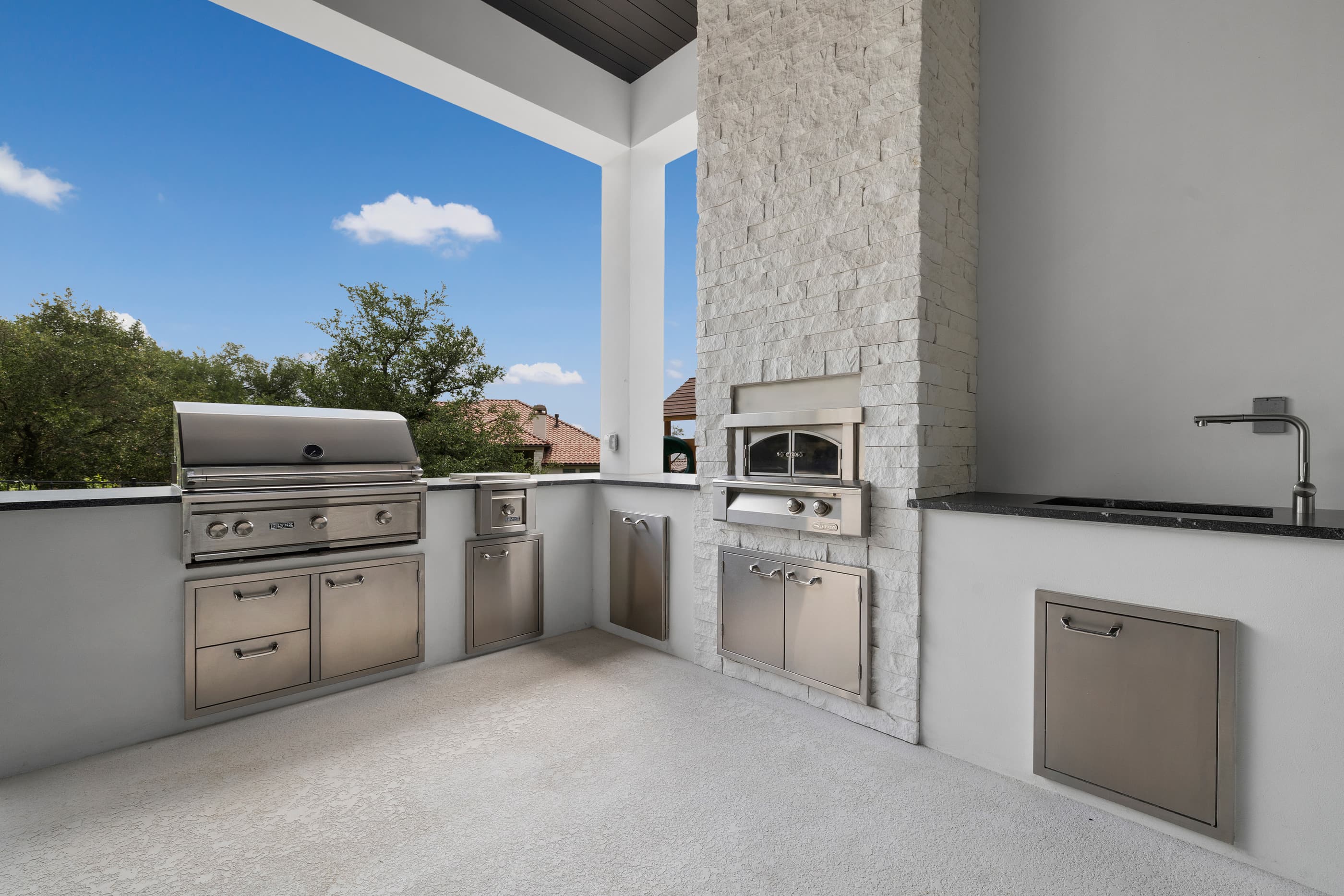 Outdoor kitchen with a built-in grill, pizza oven and stainless doors beneath a covered patio