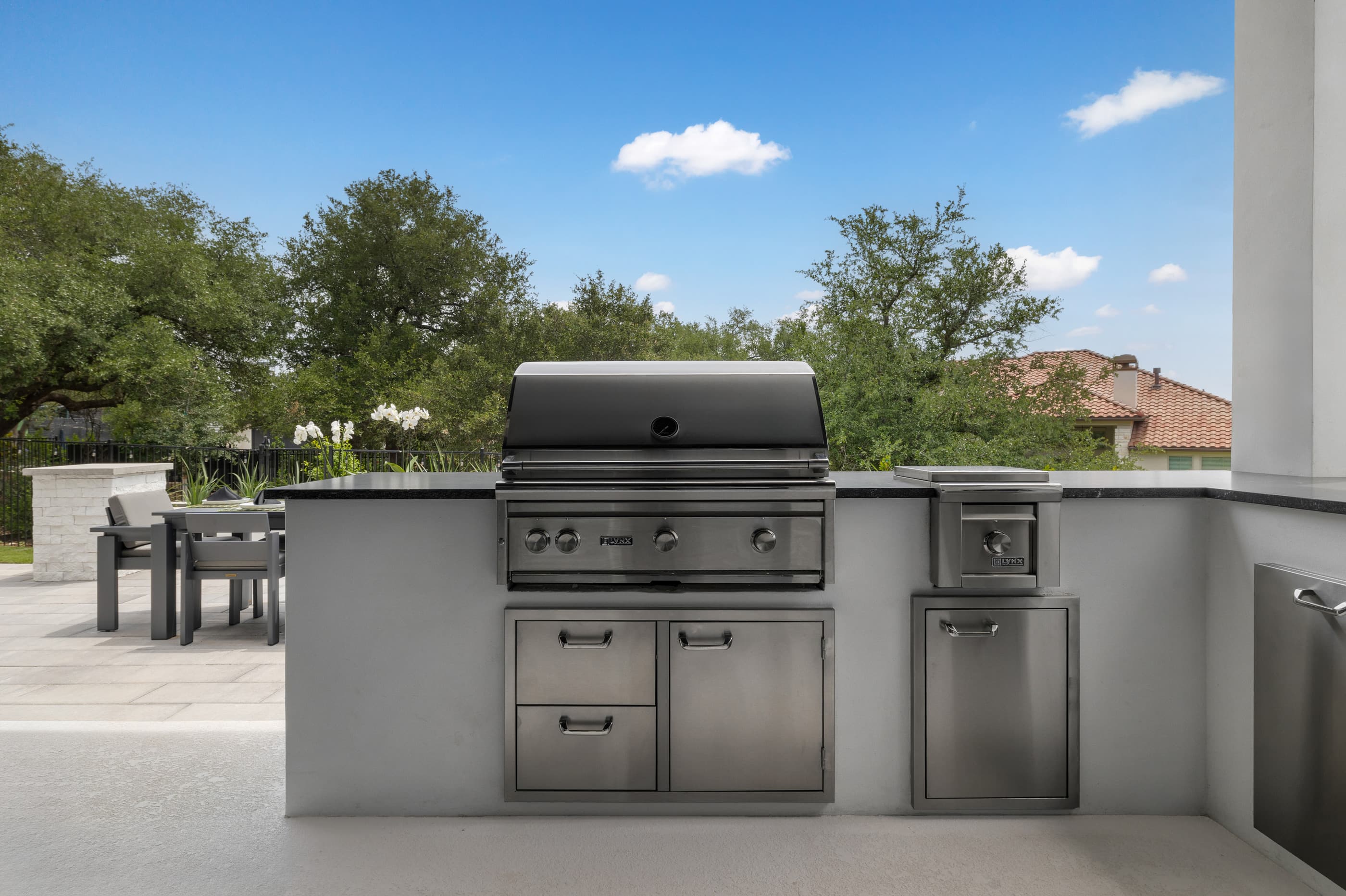 Outdoor kitchen island with a built-in grill and storage looking over an oak-shaded yard
