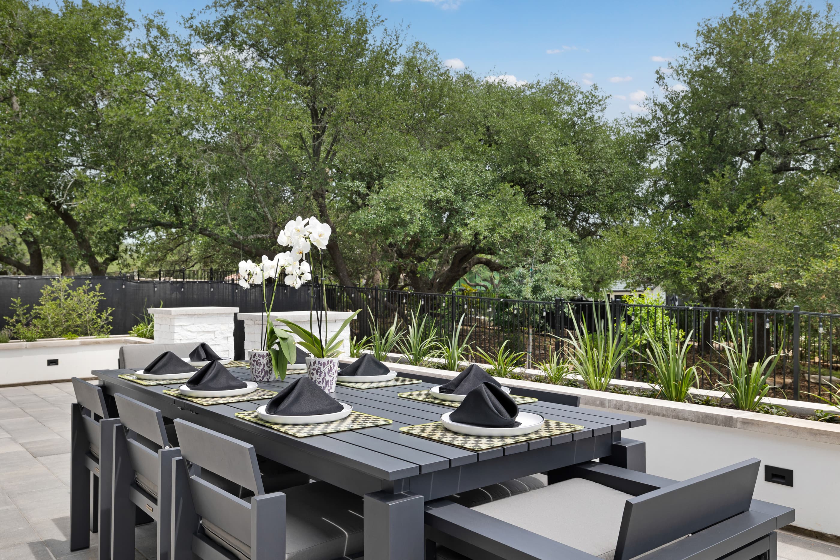 Patio dining table set for a dinner with orchids, framed by planters and mature oak trees