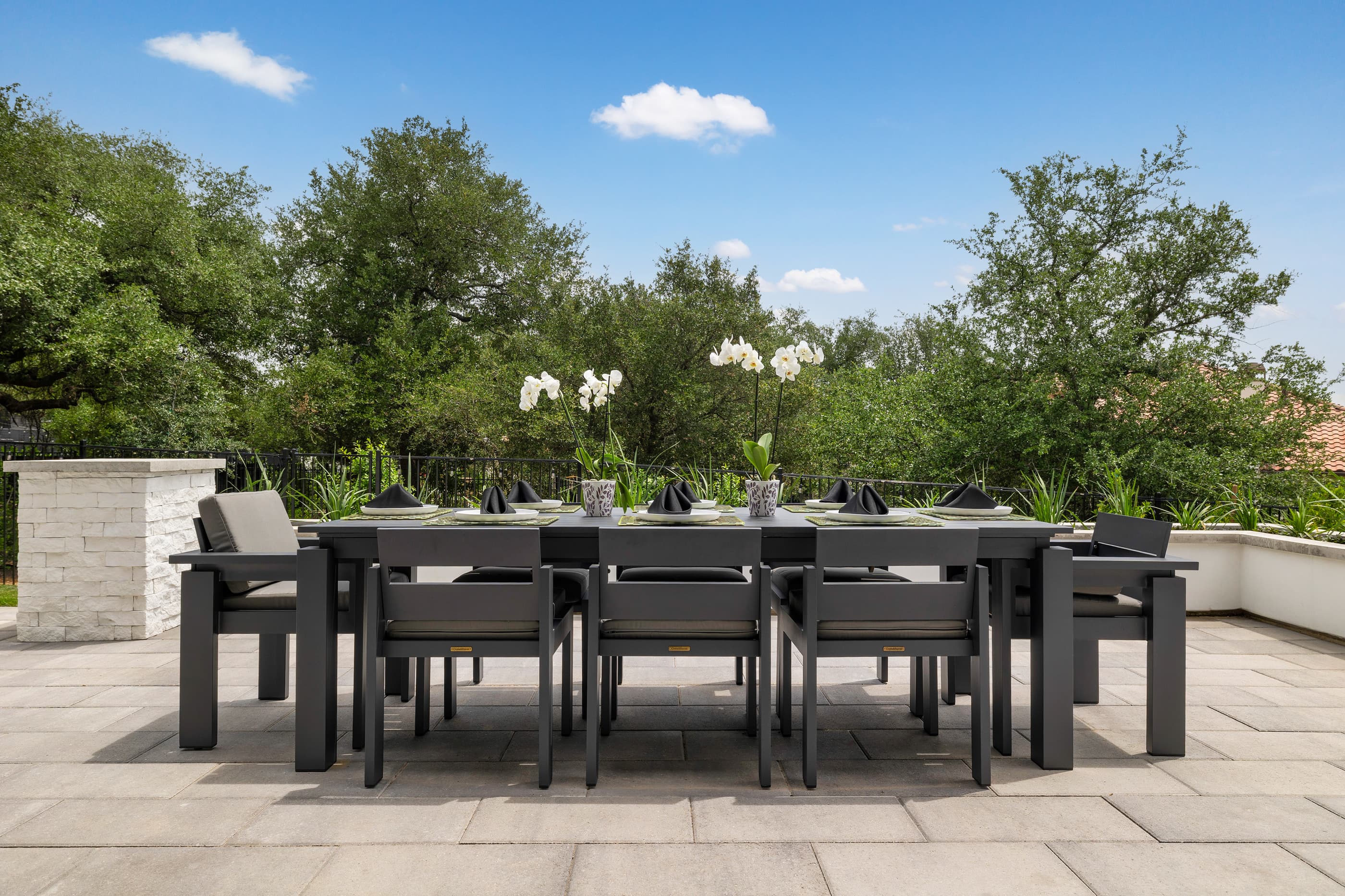 Outdoor dining table on a paver terrace under mature oak trees