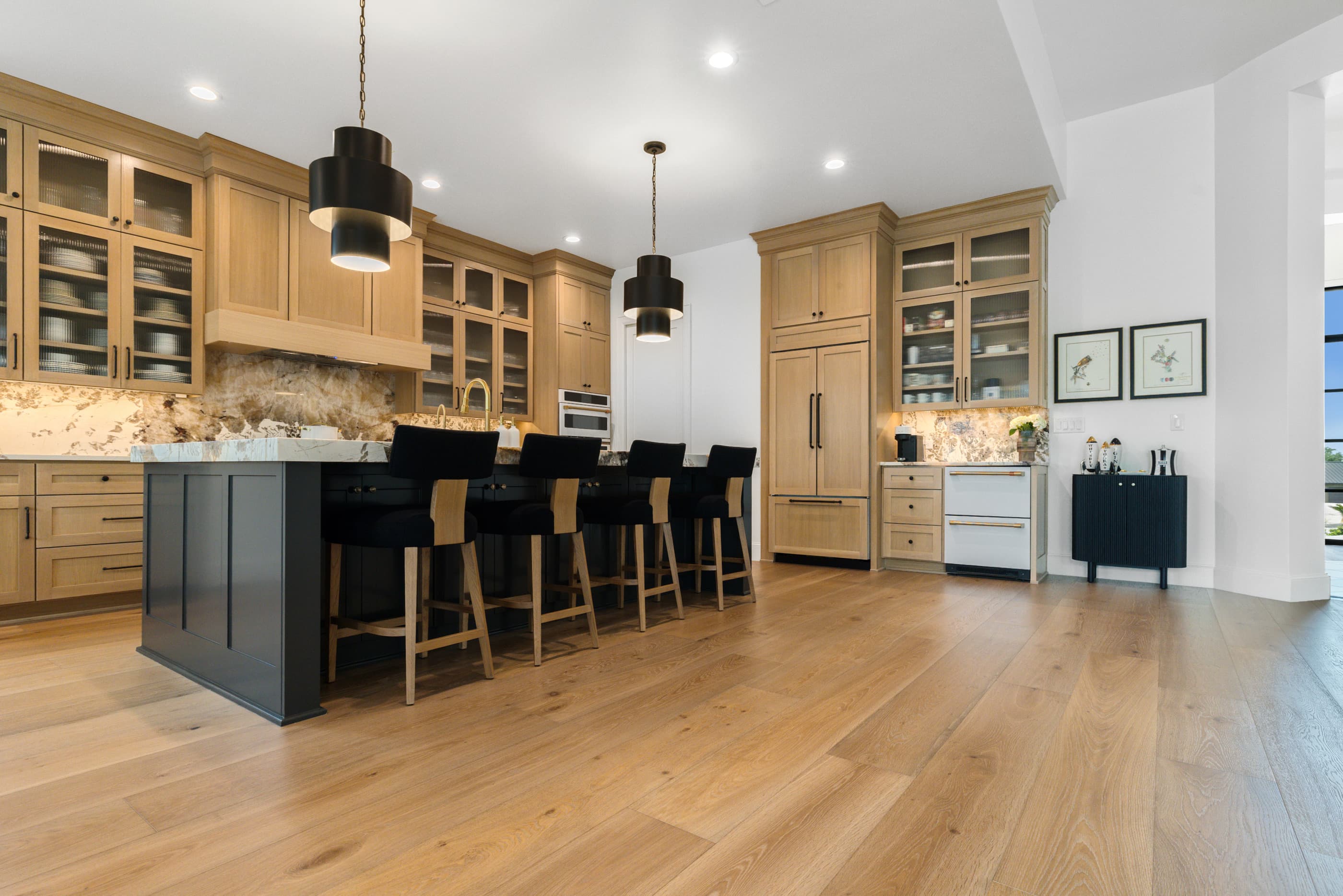 Open kitchen with a dark island, black bar stools, oak cabinets and wide-plank hardwood floors