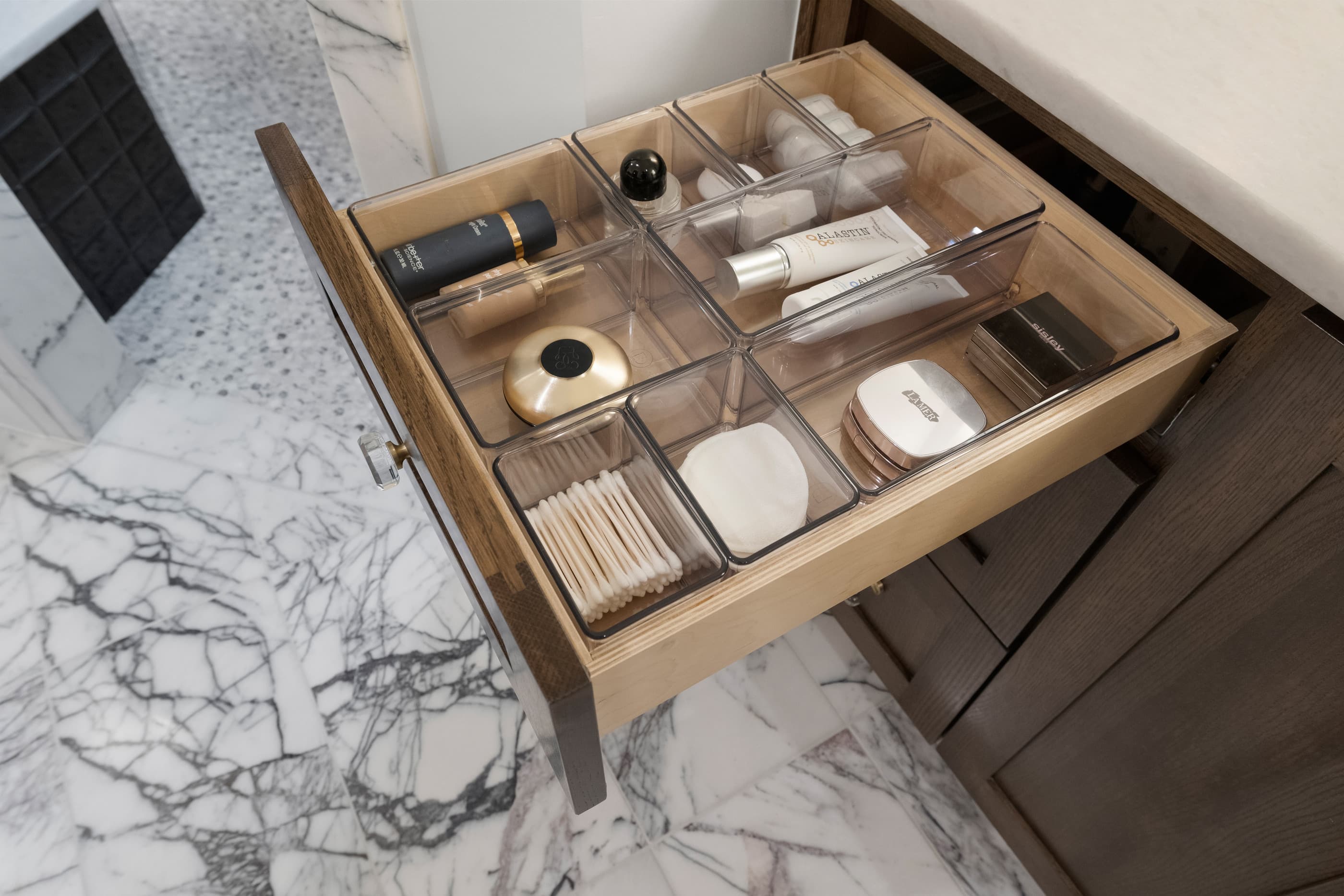 Bathroom drawer with clear organizers for cosmetics, set against a marble floor
