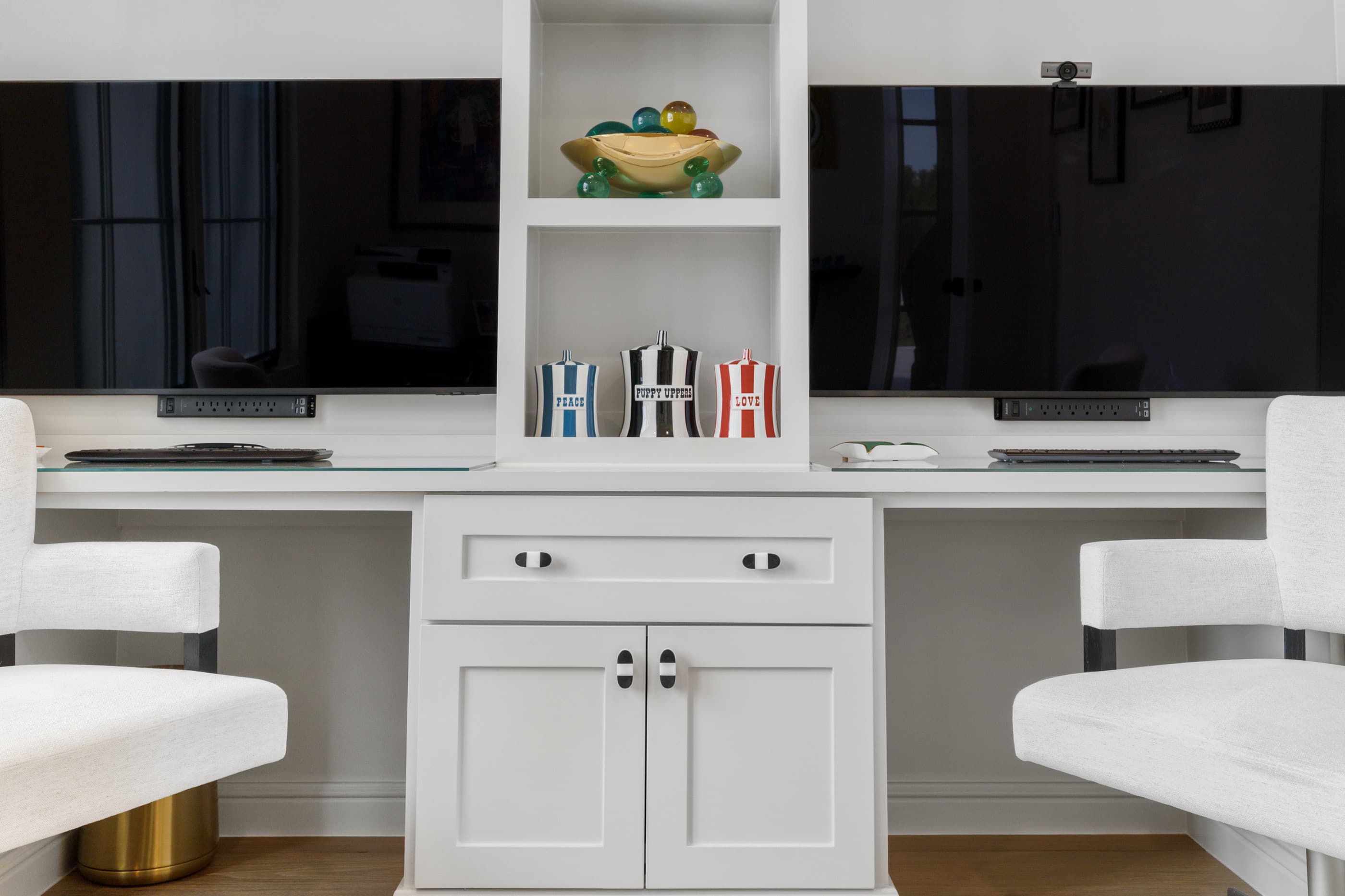 Built-in office desk with two monitors, white cabinets and open shelves