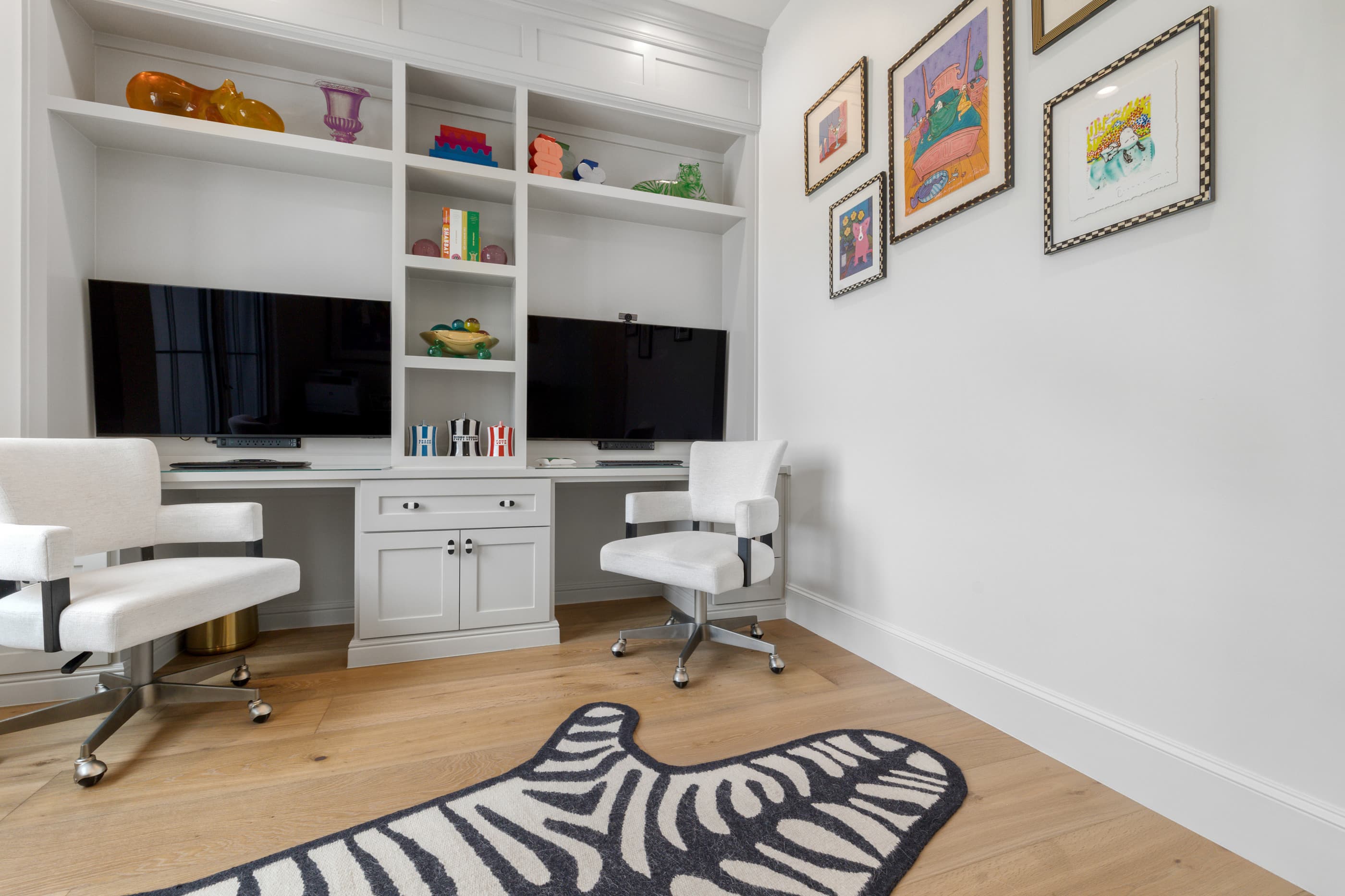 Home office with a built-in double desk, shelving, framed colorful art and a zebra-print rug