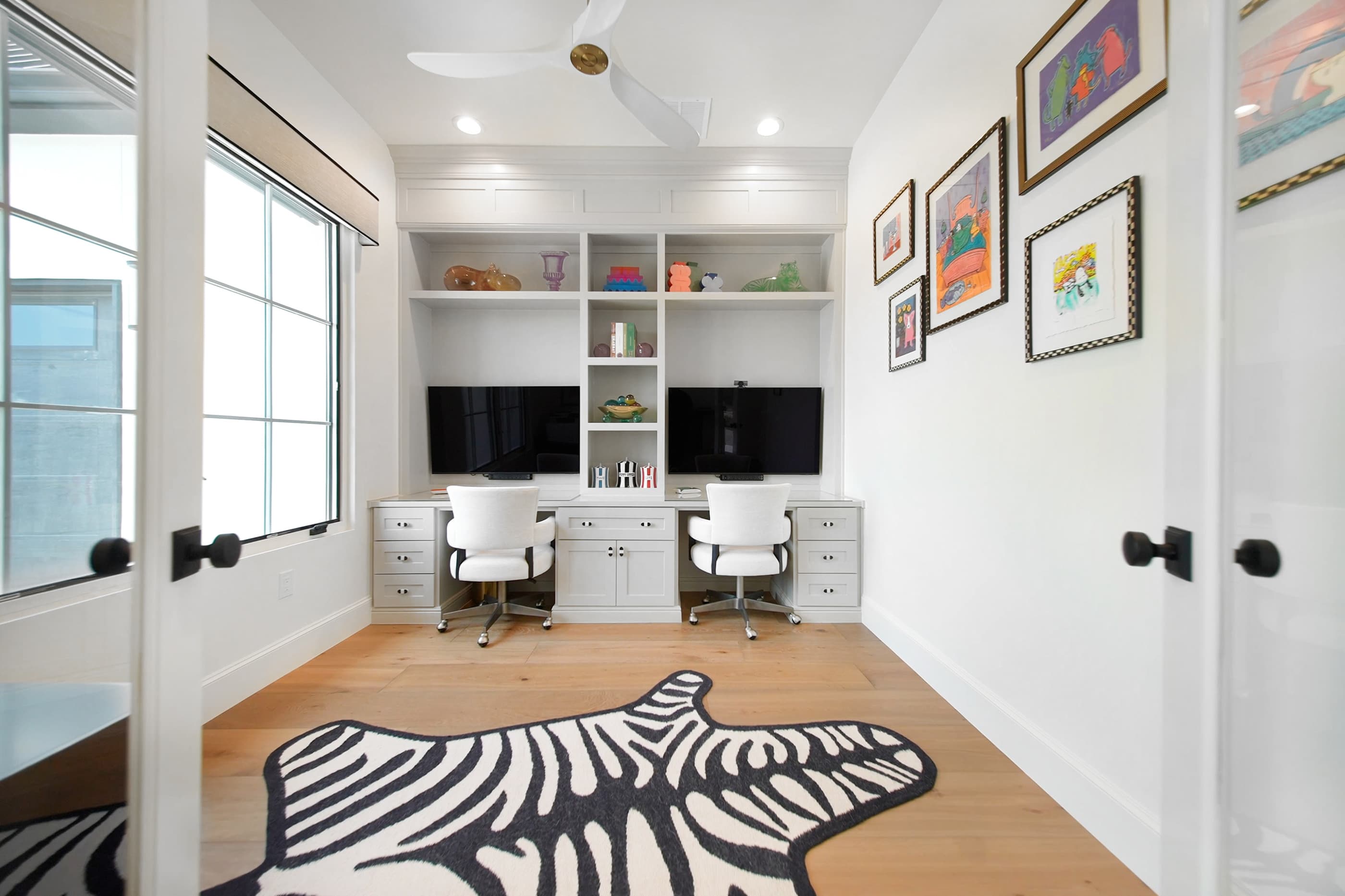 Home office with built-in desks and bookshelves, large window and gallery wall of framed art