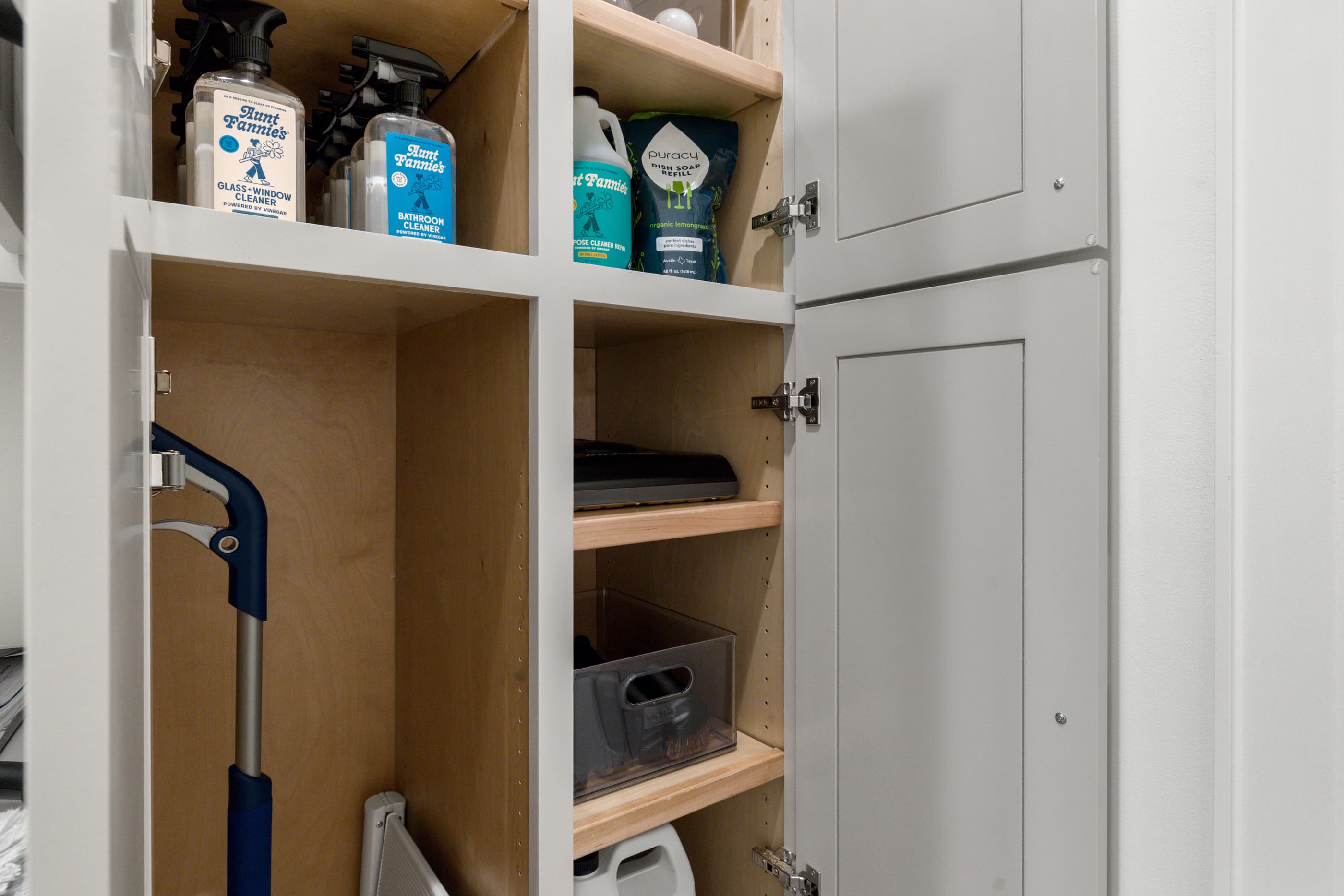 Utility closet with white shelving and a vacuum stored inside an open cabinet