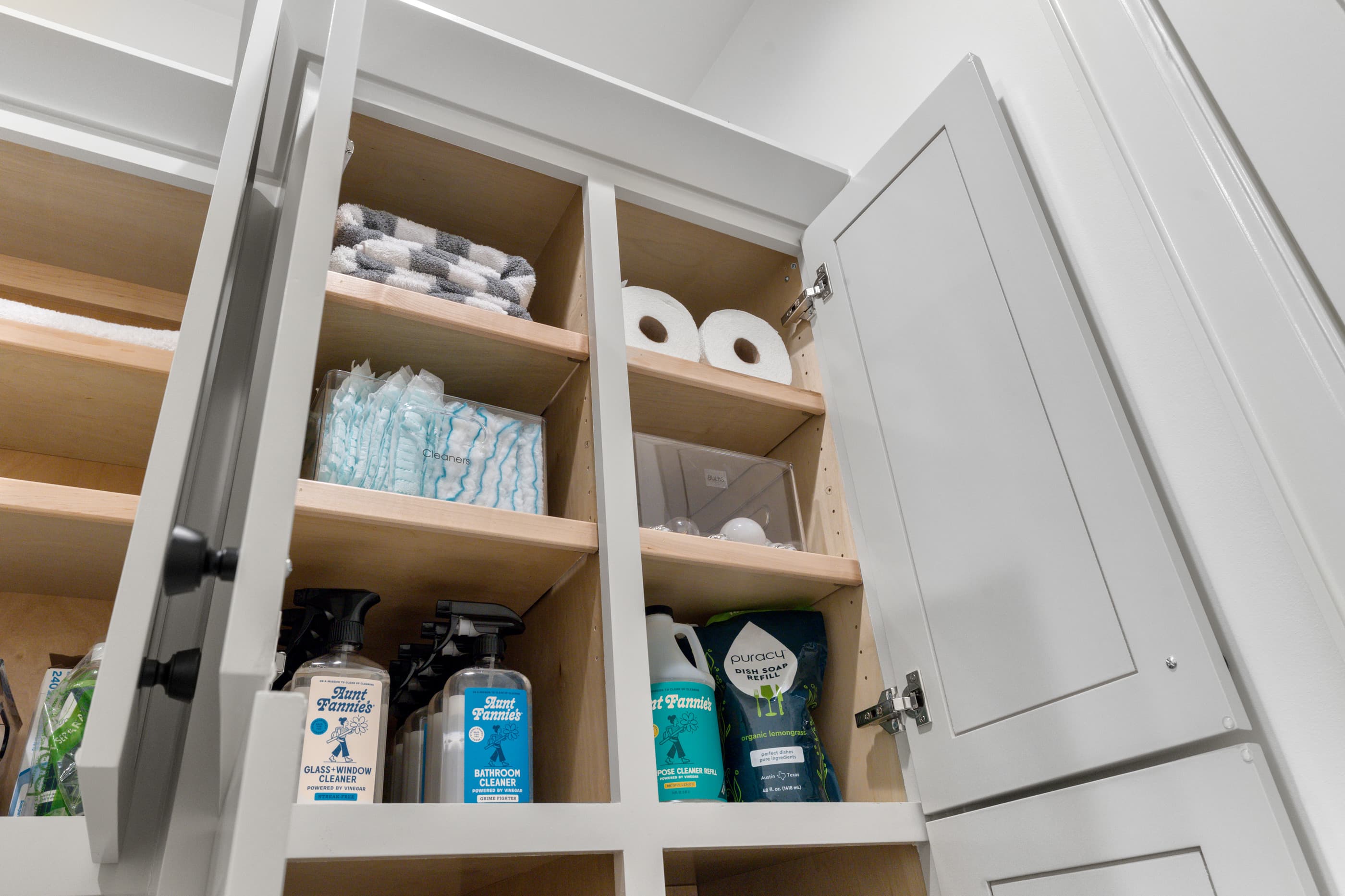 Linen and cleaning-supply storage inside a white built-in cabinet with an open door