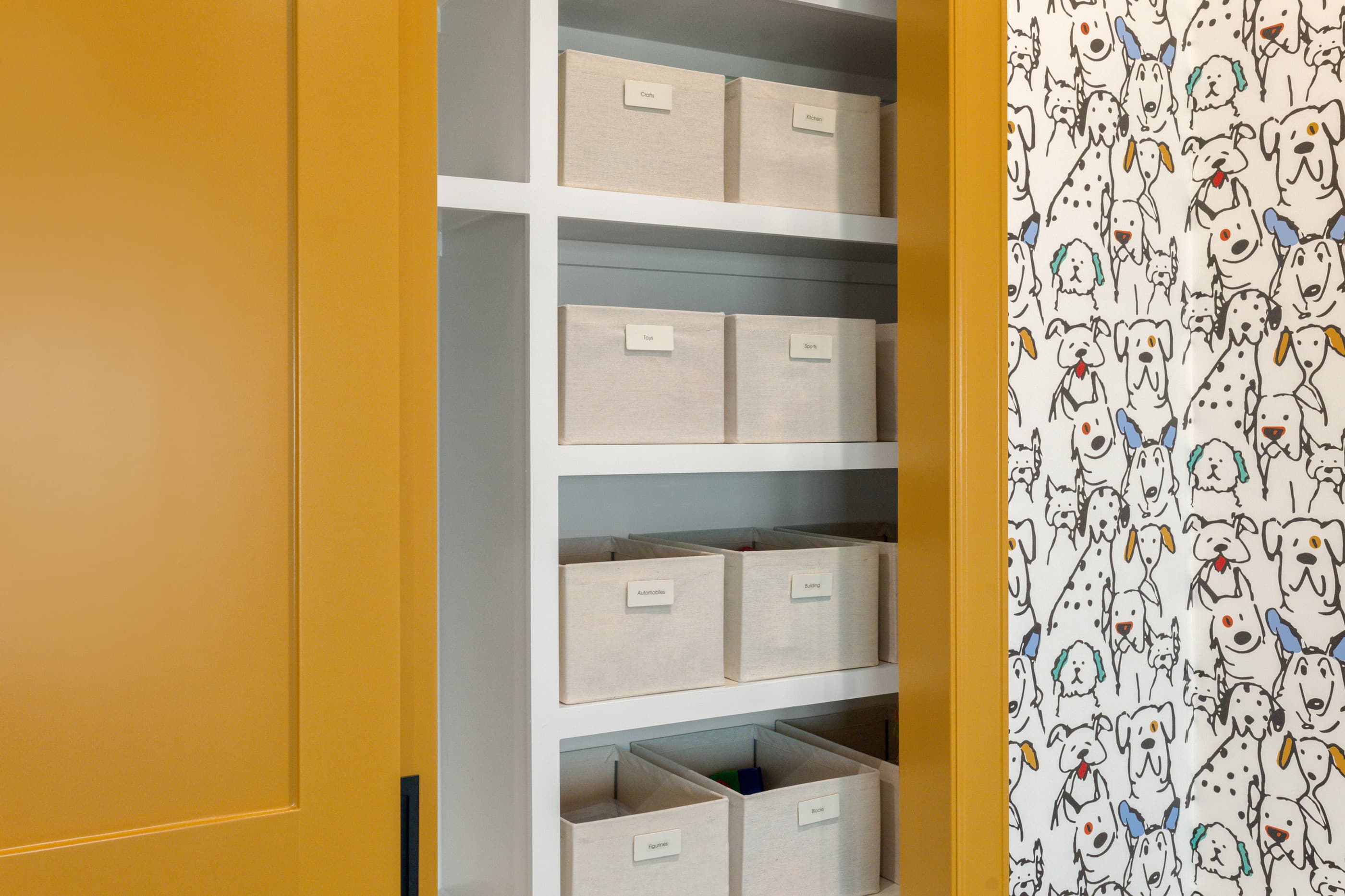 Hall linen closet with labeled fabric bins beside a mustard-yellow door and dog-print wallpaper