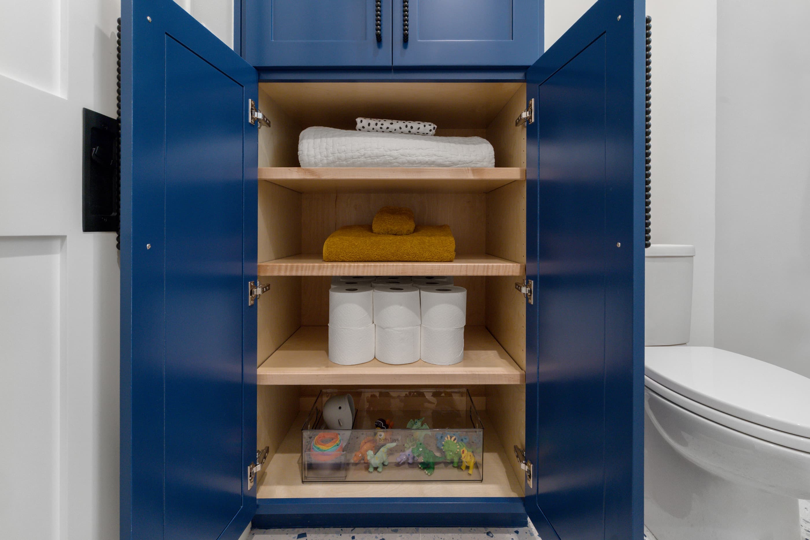 Powder room cabinet in deep blue open to show towels and supplies