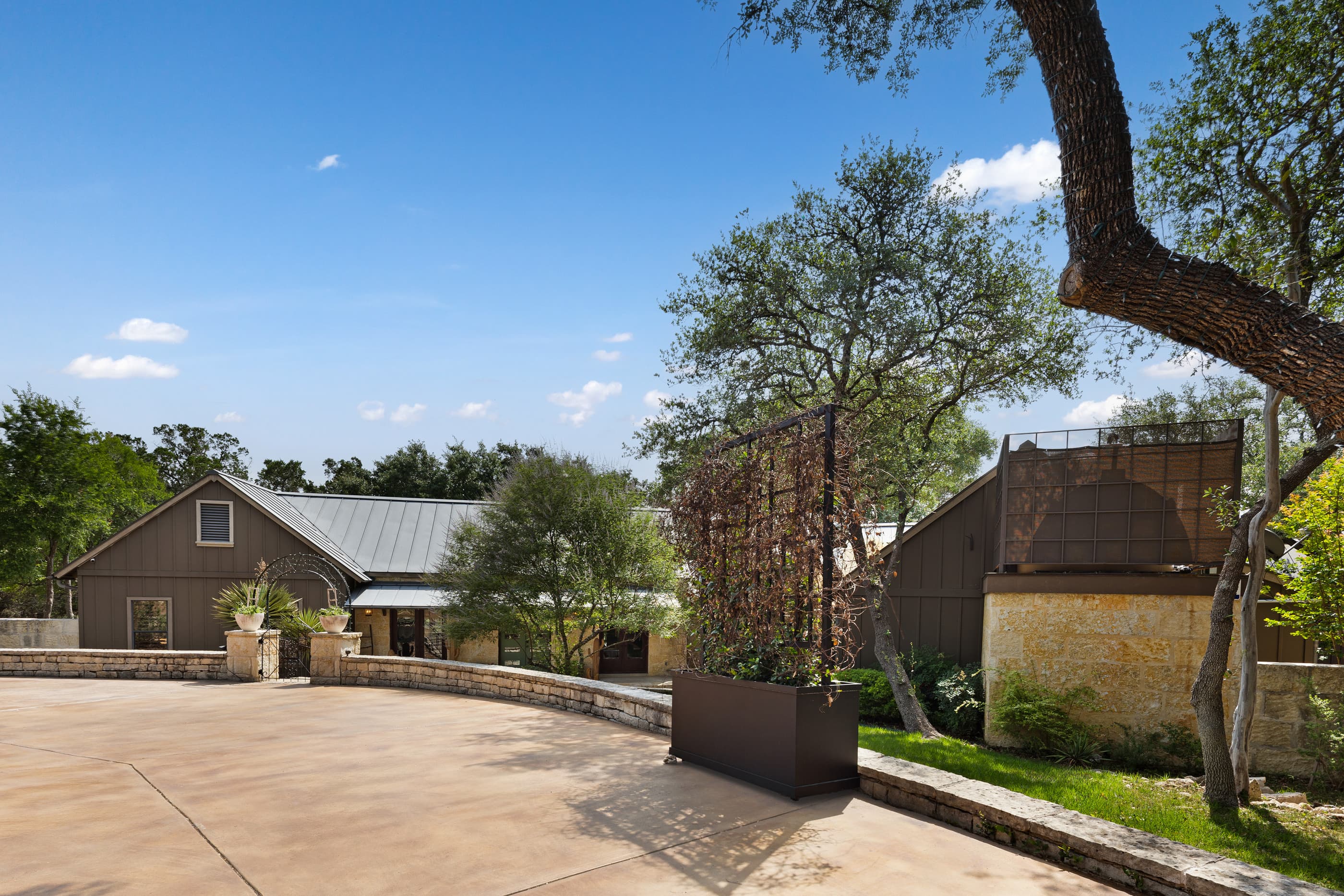 Stone-edged driveway court with mature live oaks and a rustic outbuilding